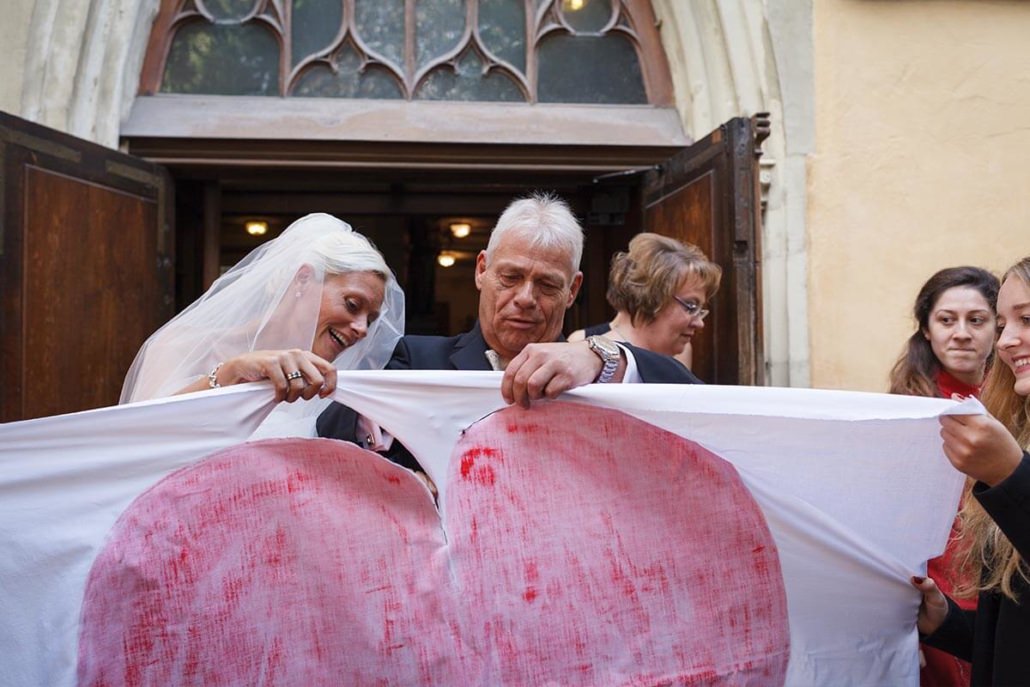 Nach der Trauung vor der Kirche schneidet das Brautpaar das Herz aus dem Bettlaken aus.