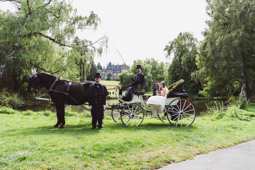 Brautpaar in Hochzeitskuttsche und Kutscher am Teisch im Schosspark mit dem Schloss von Rauischholzhausen im Hintergrund