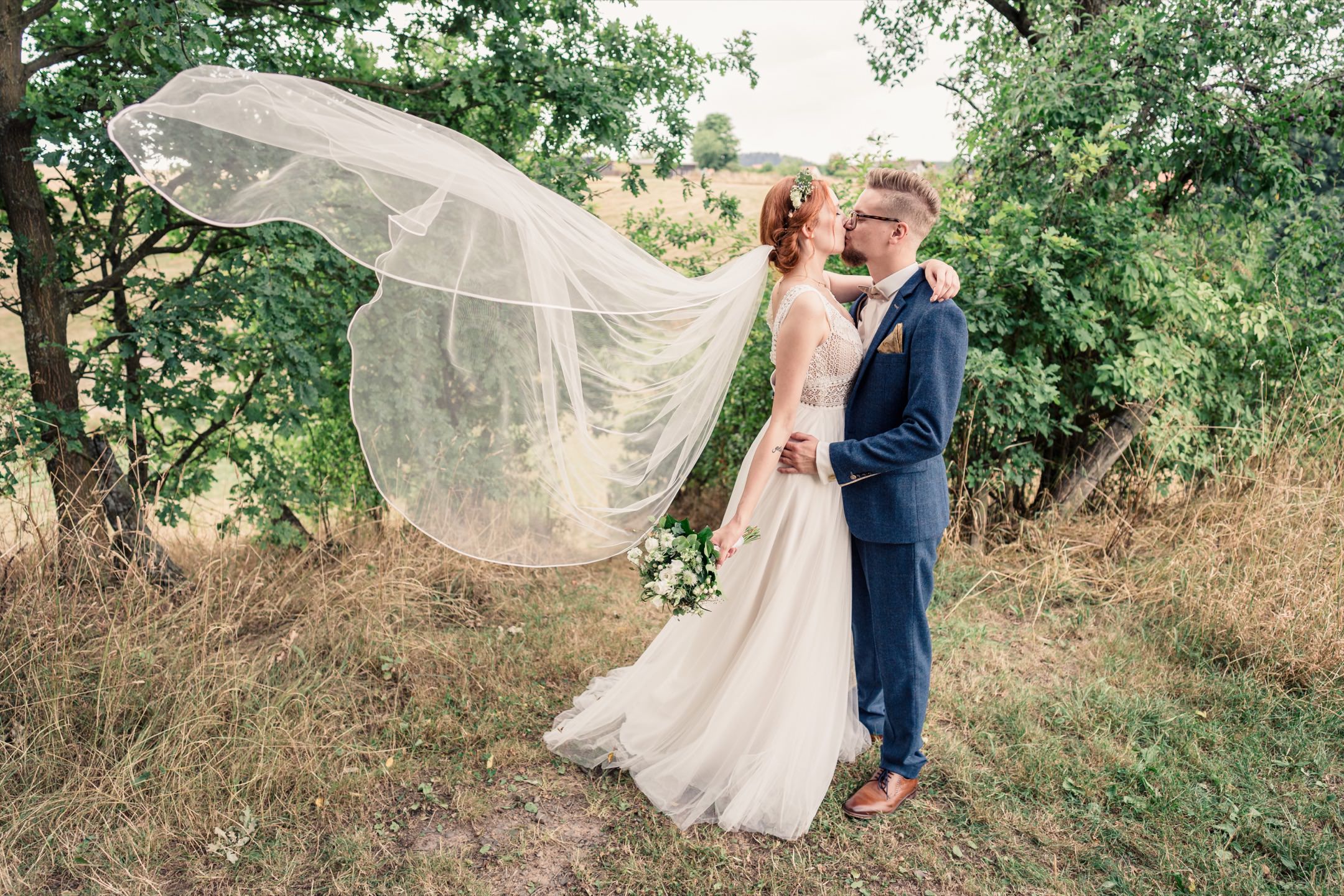 Küssendes Hochzeitspaar mit wehendem Schleier der Braut