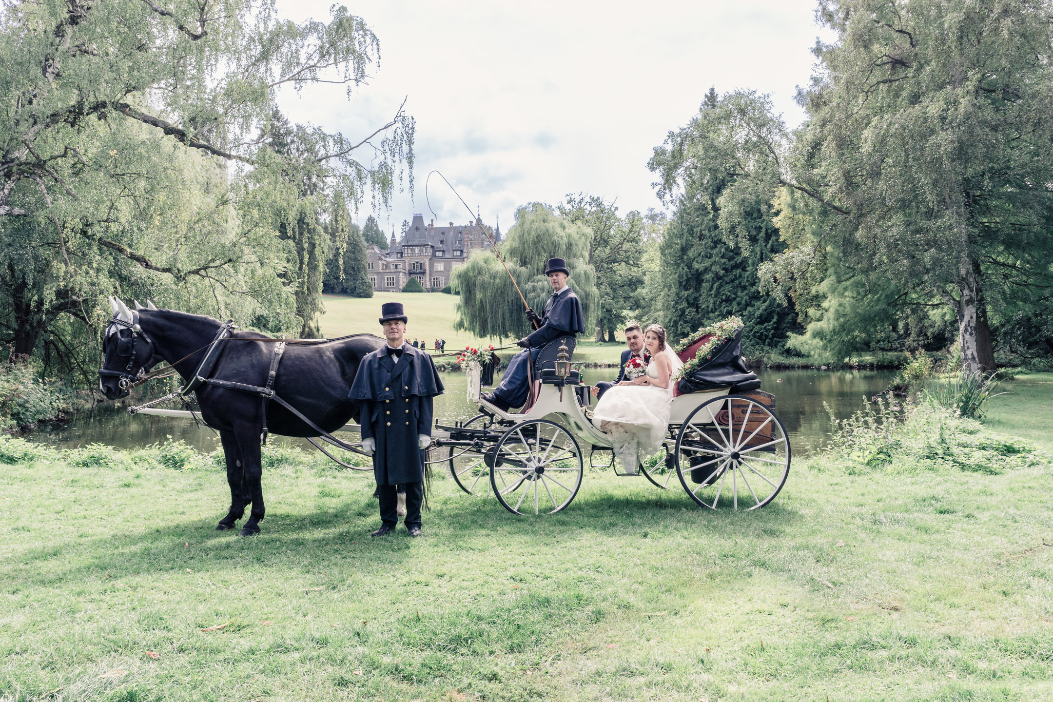 Brautpaar in Hochzeitskutsche mit Schloss im Hintergrund