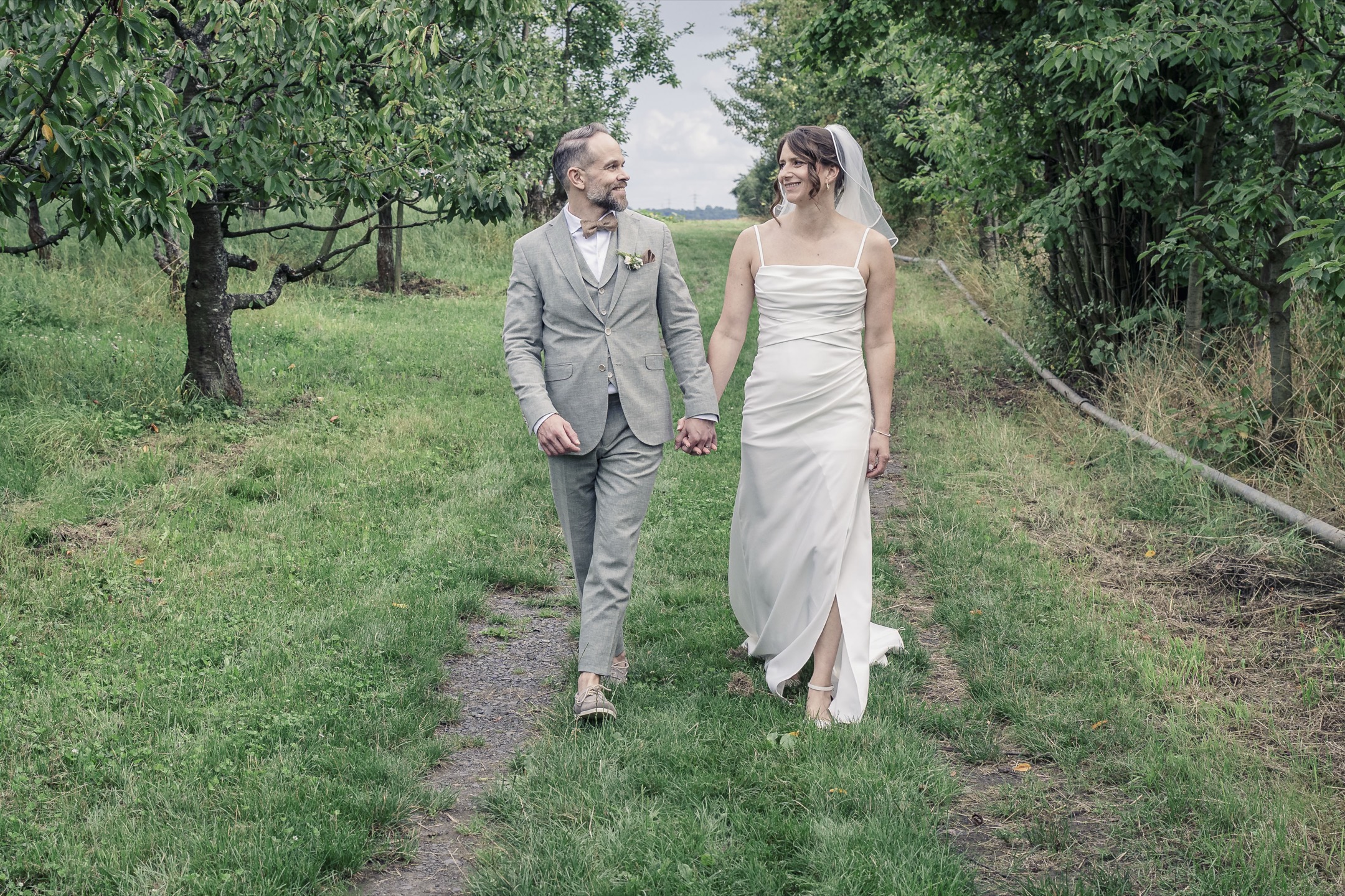 Hochzeit Obsthof am Steinberg Bad Vilbel Brautpaar spaziert Hand in Hand zwischen Apfelbäumen auf dem Obsthof am Steinberg in Bad Vilbel – Hochzeitsfotograf Frankfurt Rhein-Main