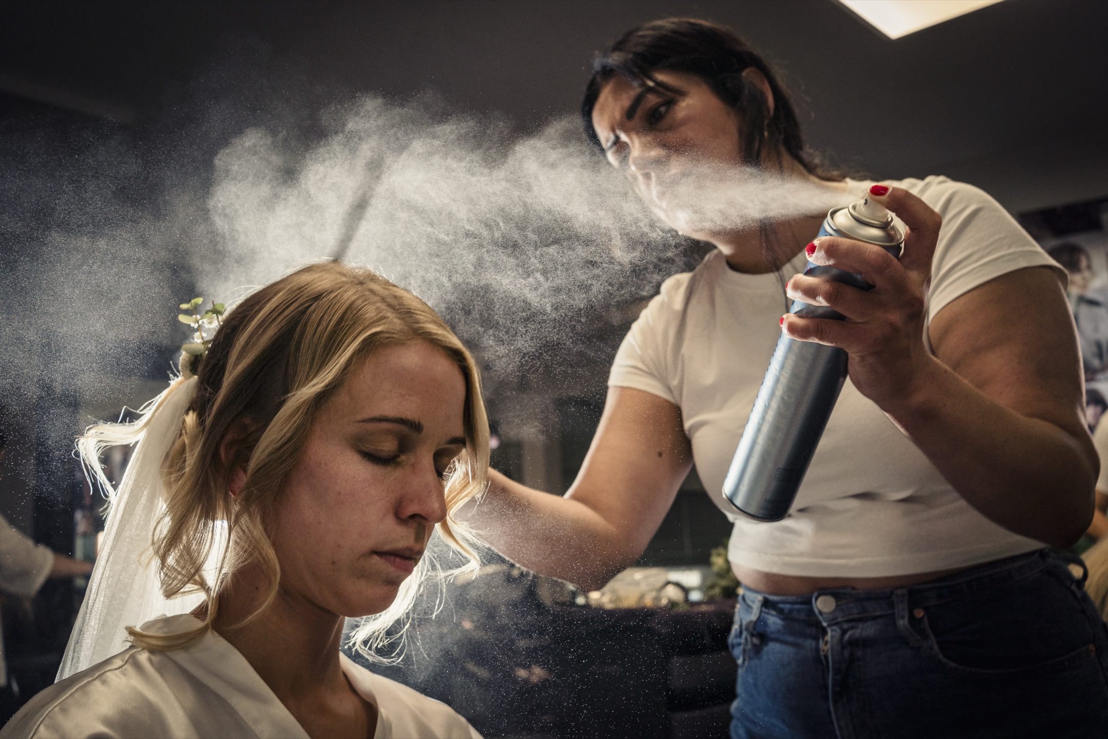 Braut beim Getting Ready, Visagistin fixiert die Frisur mit Haarspray